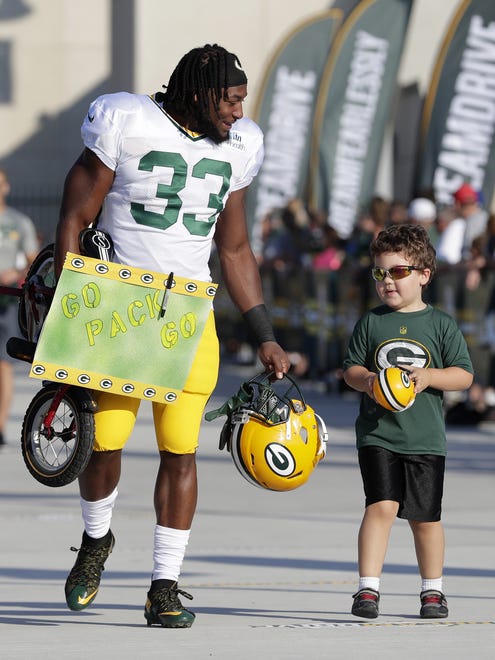 Green Bay Packers running back Aaron Jones (33) carries a young fan's bike to training camp practice on Aug. 1, 2017, at Ray Nitschke Field.